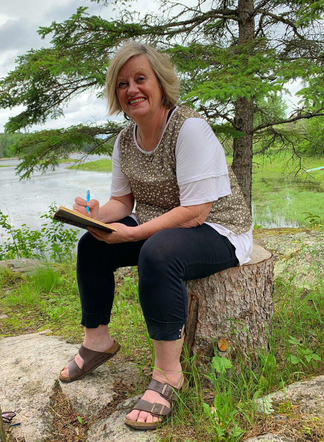 Leanne Fournier, sitting in nature on a log, with journal in hand.